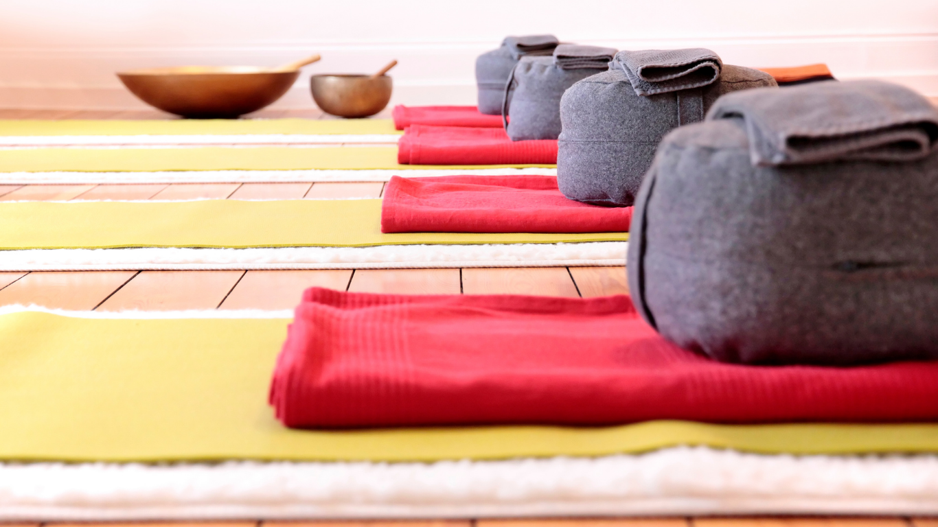 Yoga mat, bolster, blanket, and eye pillow set up for a sound healing session