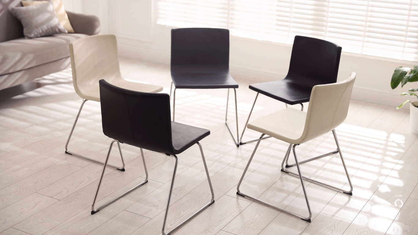 Empty grief support group circle with chairs arranged thoughtfully, a blanket, tissues, and a candle at the center