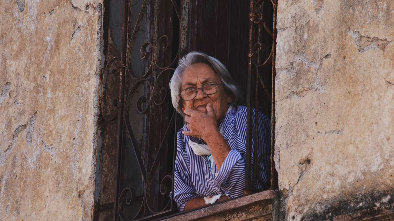 An older woman seated by a window in soft morning light, reflecting on spousal loss