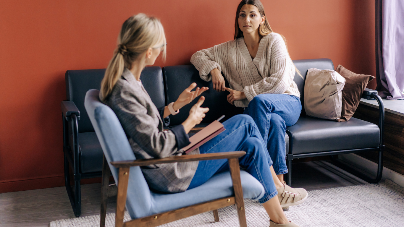 A grief therapist in conversation with a client in a warm light-filled office, spousal grief counseling Bergen County NJ