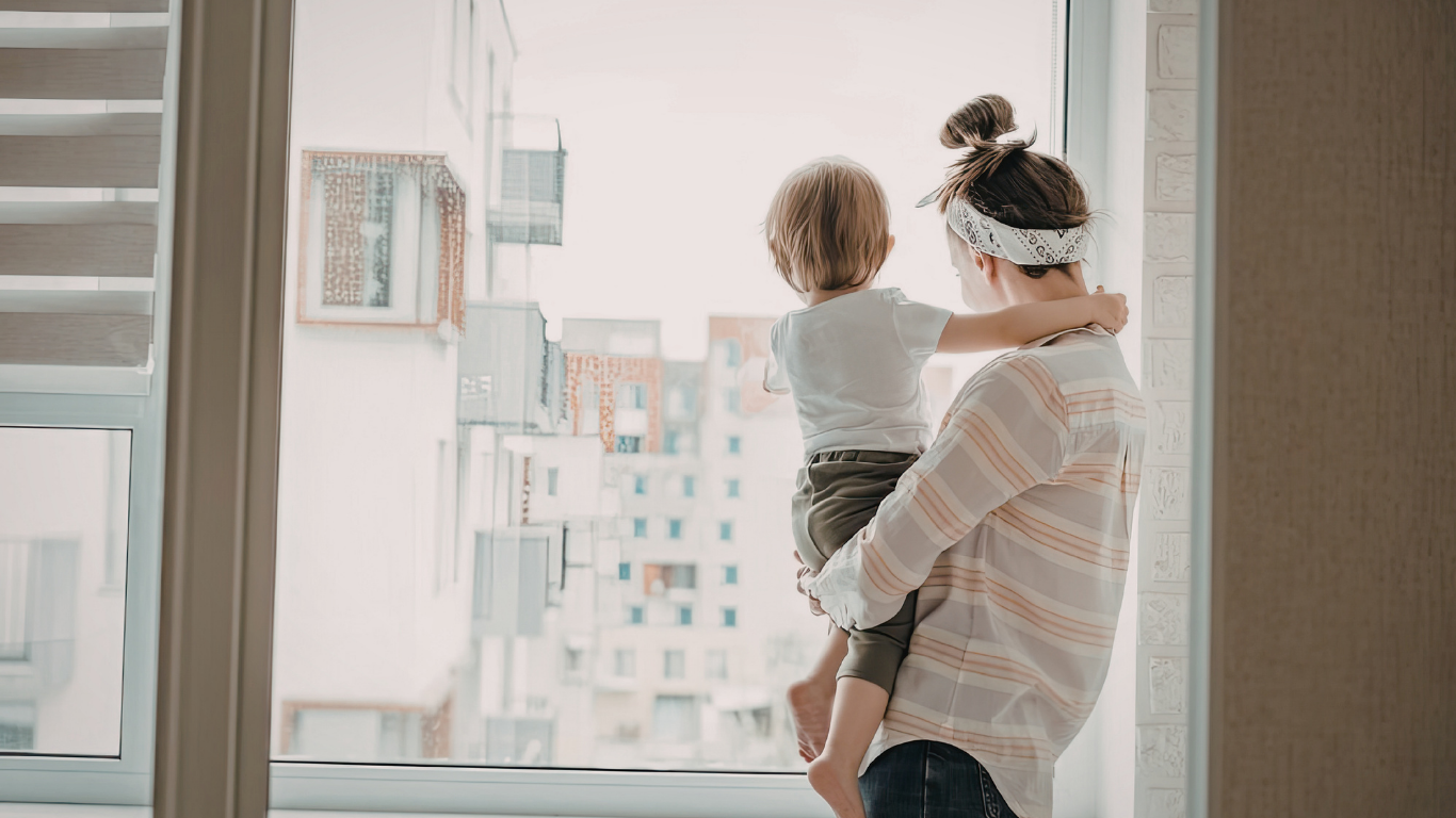 A parent and child standing quietly together, looking out a window — a tender shared moment in grief