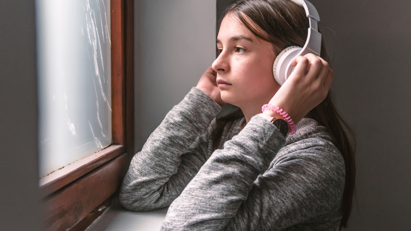 A teenager sitting by a window with headphones, contemplative — adolescent grief Bergen County
