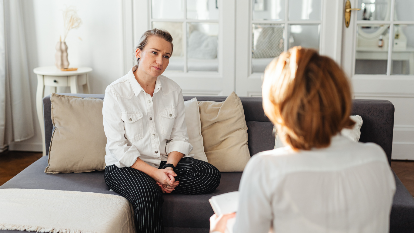 Person sitting thoughtfully before a grief counseling first appointment, hands folded, soft indoor light